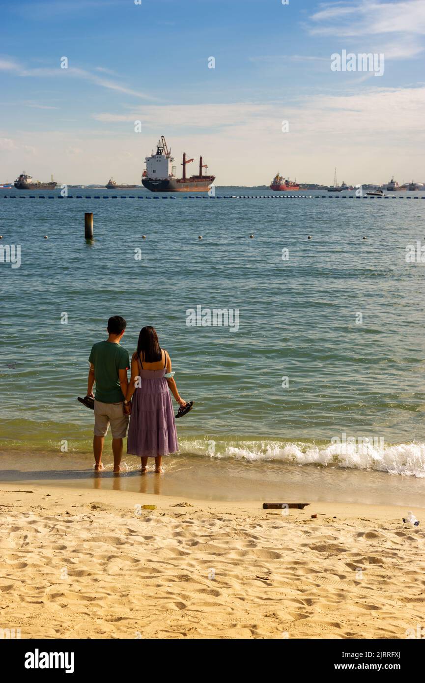 Détente sur la plage de Siloso avec des navires à conteneurs ancrés au large, île de Sentosa, Singapour Banque D'Images
