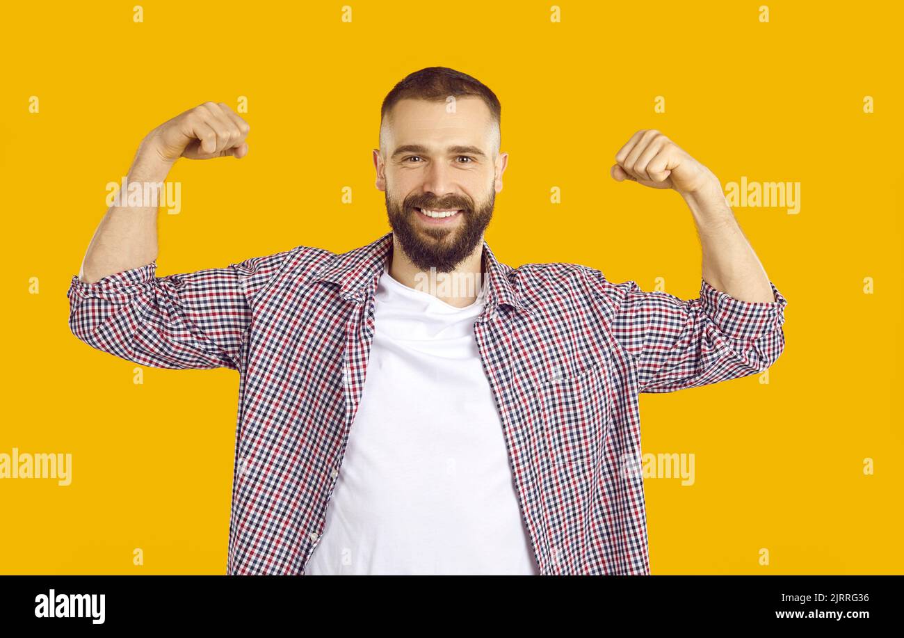 Homme joyeux montre en plaisantant biceps démontrant sa force sur fond orange. Banque D'Images