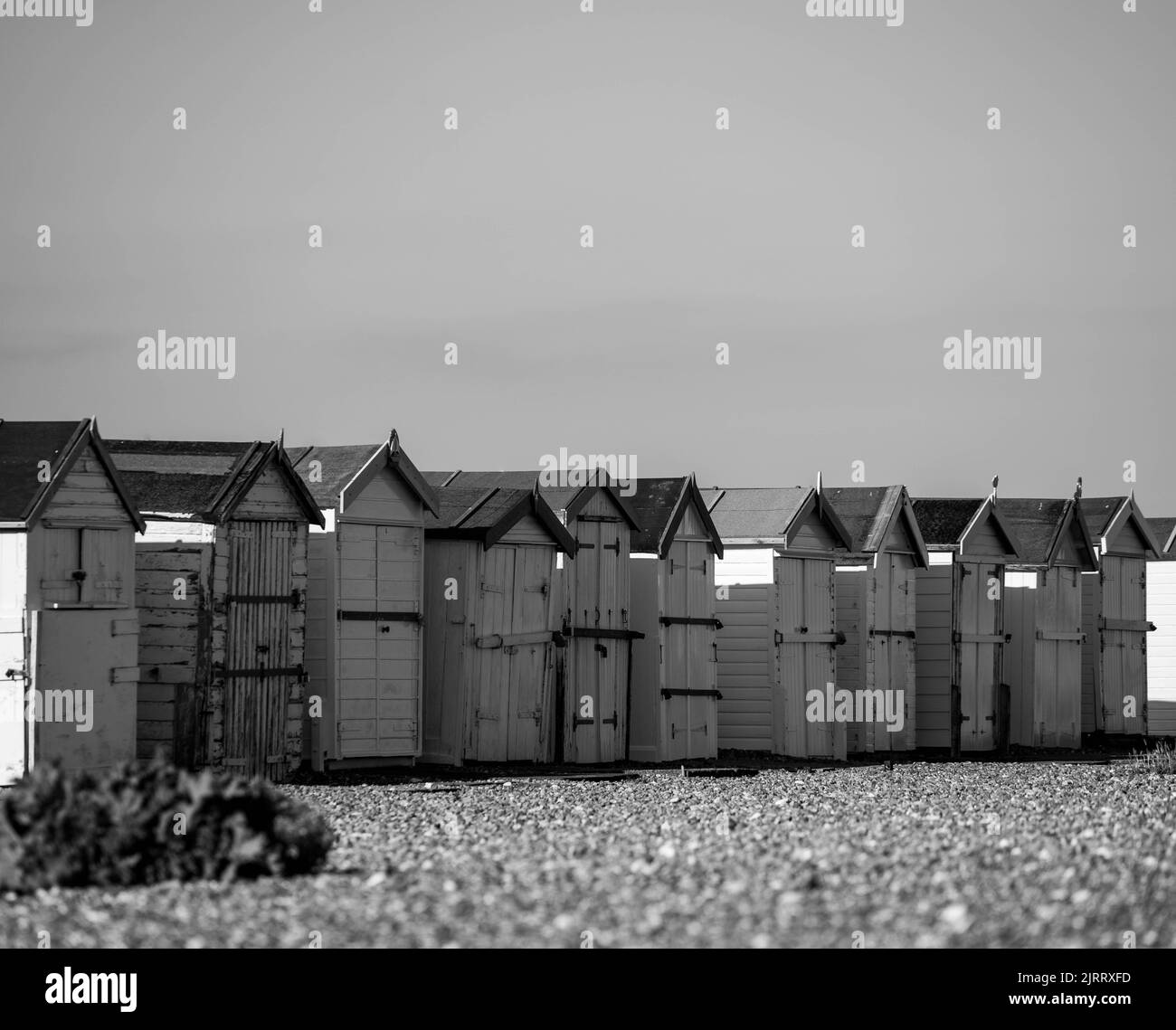 Photographie en noir et blanc de huttes de plage sur une plage de galets avec une usine de plage en premier plan à worthing West sussex Banque D'Images