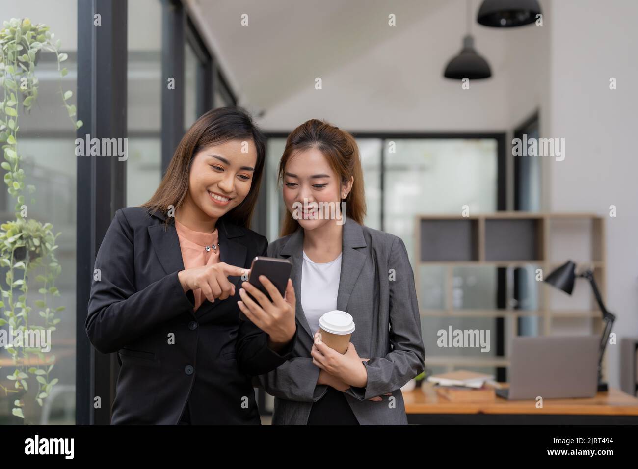 Deux femmes d'affaires asiatiques discutent de données sur téléphone mobile. Se conseillant dans le bureau, Banque D'Images
