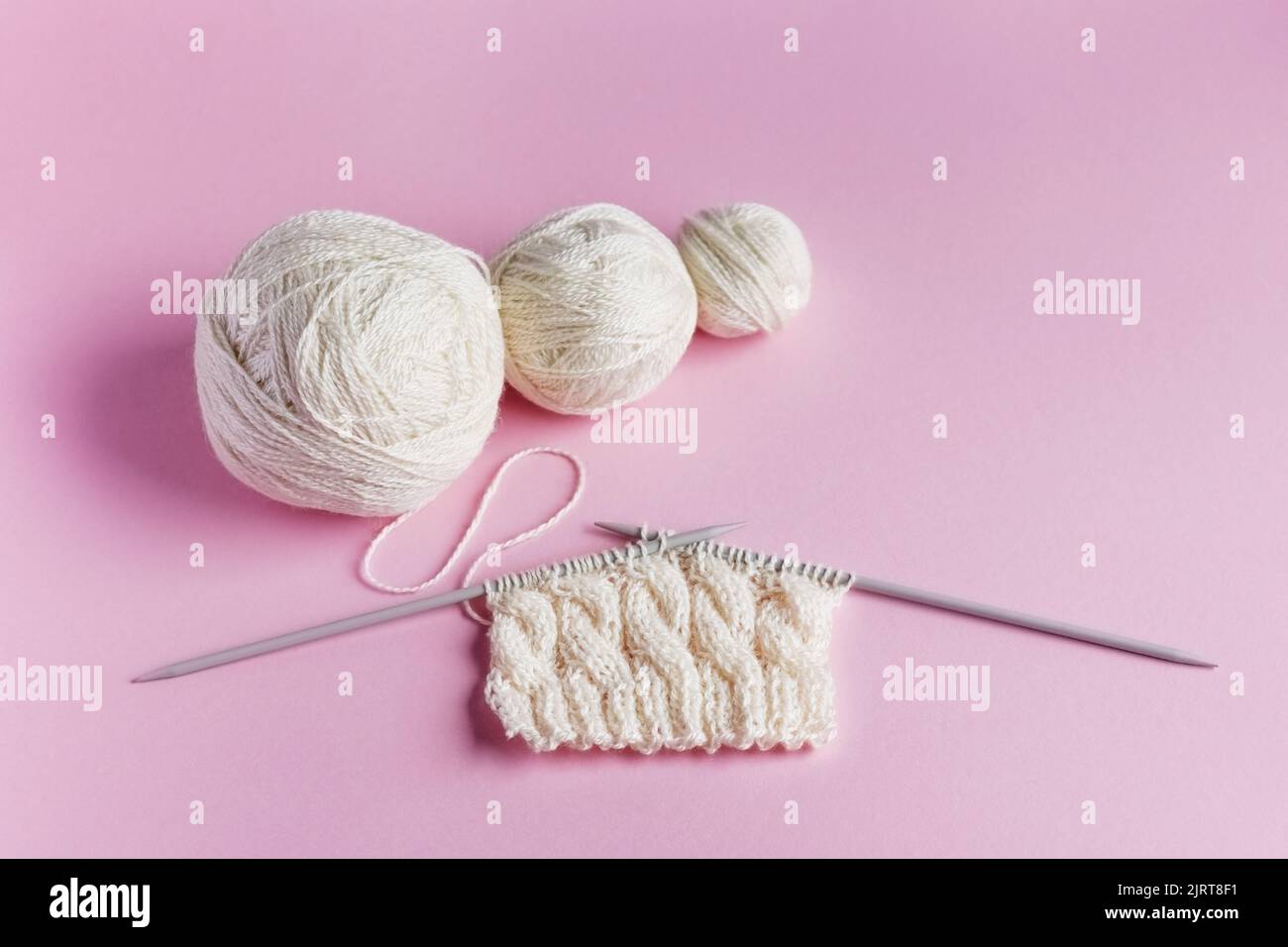 Boules blanches de fil avec aiguilles à tricoter dans un sac à ficelle sur un fond lilas pour tricoter des vêtements chauds, passe-temps Banque D'Images