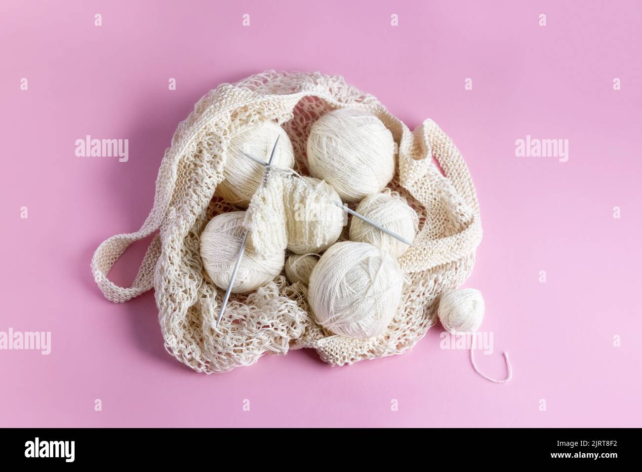 Boules blanches de fil avec aiguilles de tricotage dans un sac à ficelle sur un fond rose pour tricotage de vêtements chauds, passe-temps. Vue d'ensemble Banque D'Images