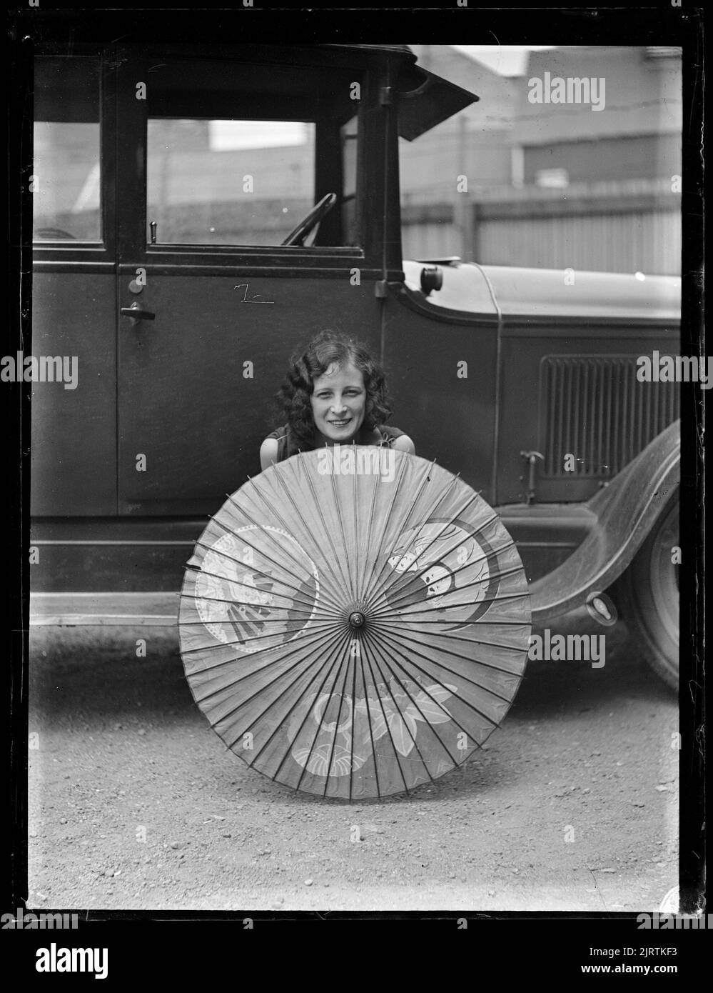 Femme assise à bord d'une voiture de course, derrière un parasol à ciel ouvert, sur l'île du Nord, par Leslie Adkin. Banque D'Images