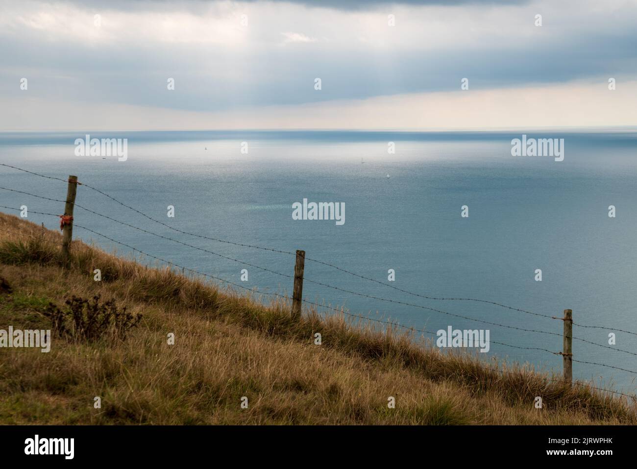 Paysage marin sombre et spectaculaire sur une falaise de la côte jurassique, Dorset, Angleterre, Royaume-Uni avec herbe balayée par le vent et poste de clôture et des éclats de lumière du soleil sur la mer Banque D'Images