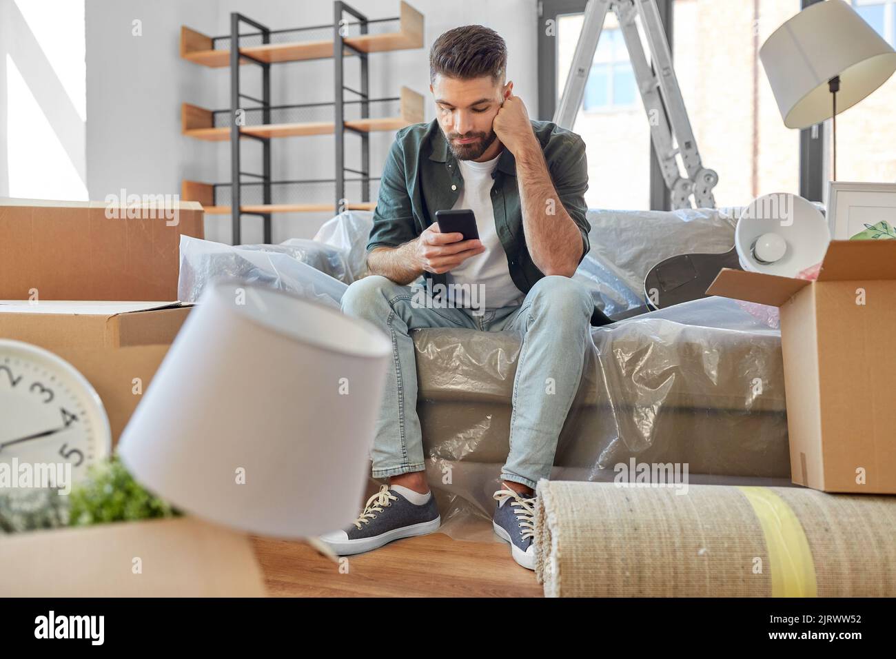 triste homme avec un smartphone et des boîtes de déménagement à la maison Banque D'Images