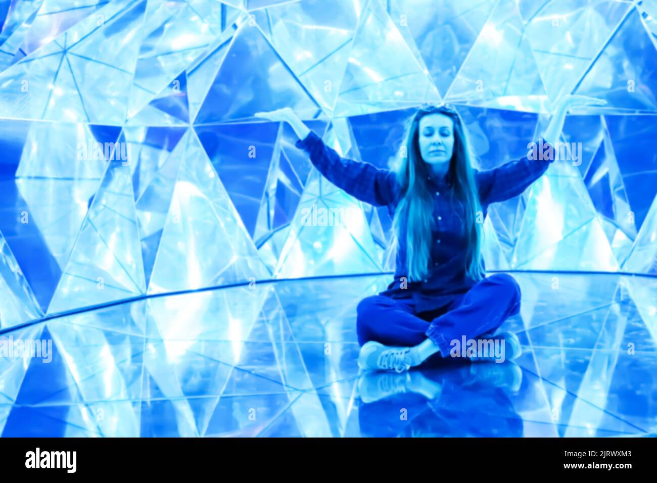 Une femme est assise dans une position lotus dans une salle lumineuse en cristal. Image floue Banque D'Images