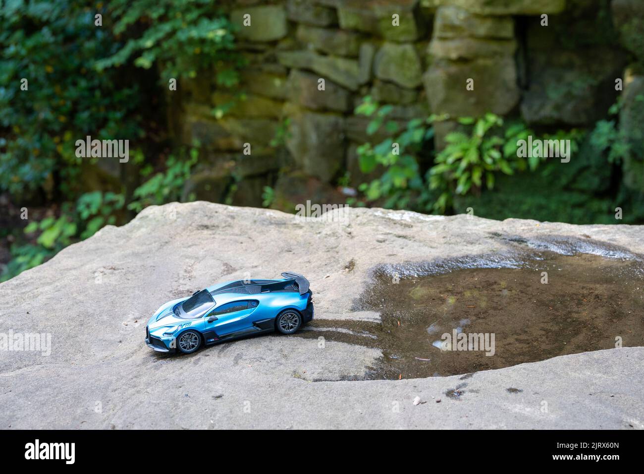 Modèle de voiture de course métallique bleu Bugatti, dans une scène de nature, sur un rocher, en sortant d'une flaque d'eau. Banque D'Images