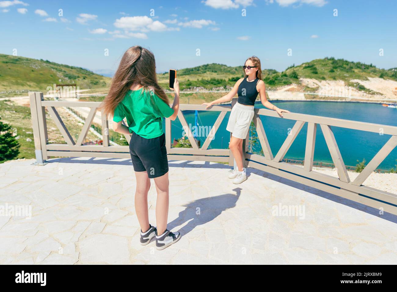 Jeunes filles prenant des photos avec le téléphone les unes des autres. Jeunes filles touristiques sur la montagne au bord du lac Banque D'Images