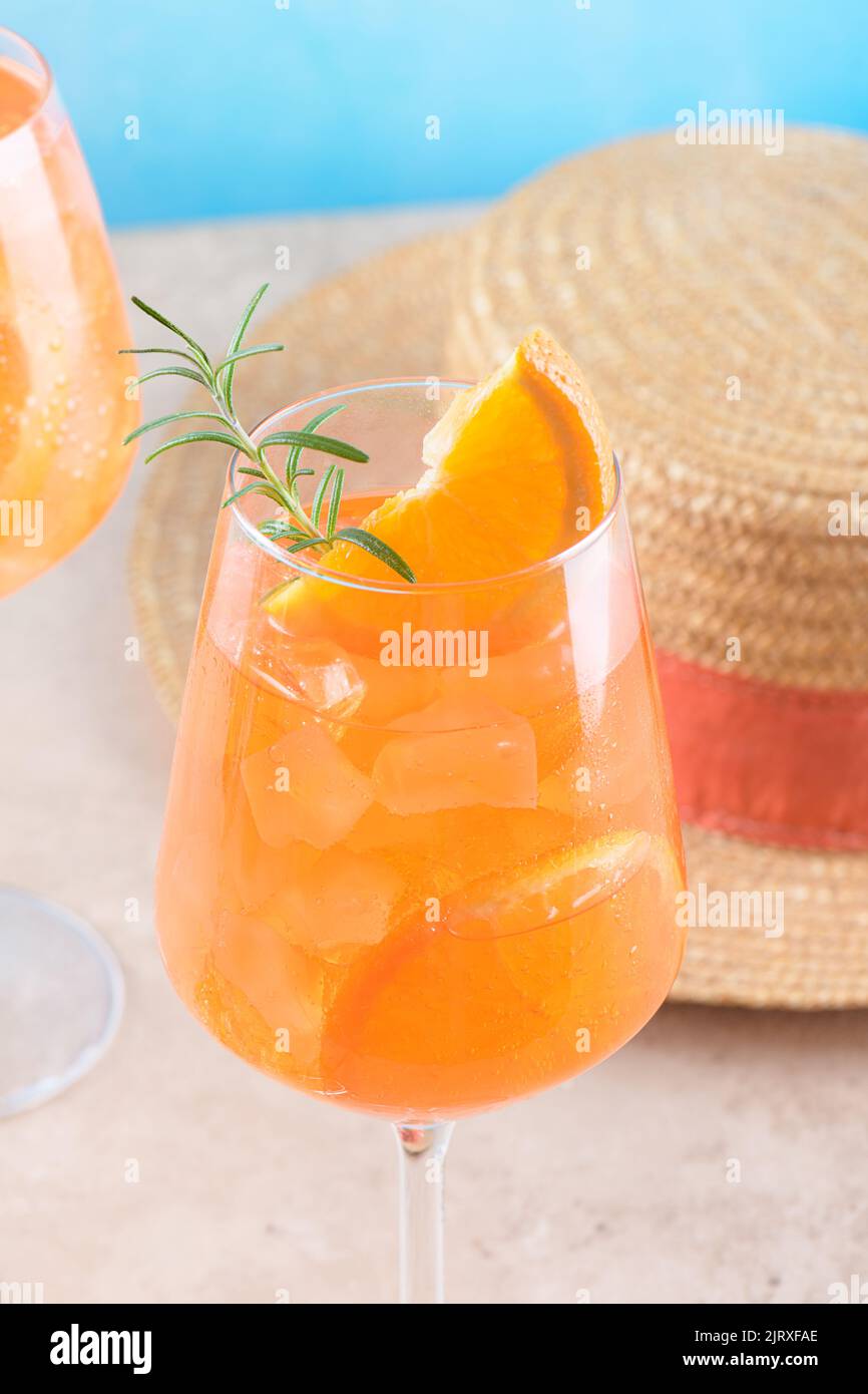 Apéritif italien apéritif apéritif apéritif au verre avec glace, tranche d'orange et chapeau de paille sur fond de pierre beige Banque D'Images