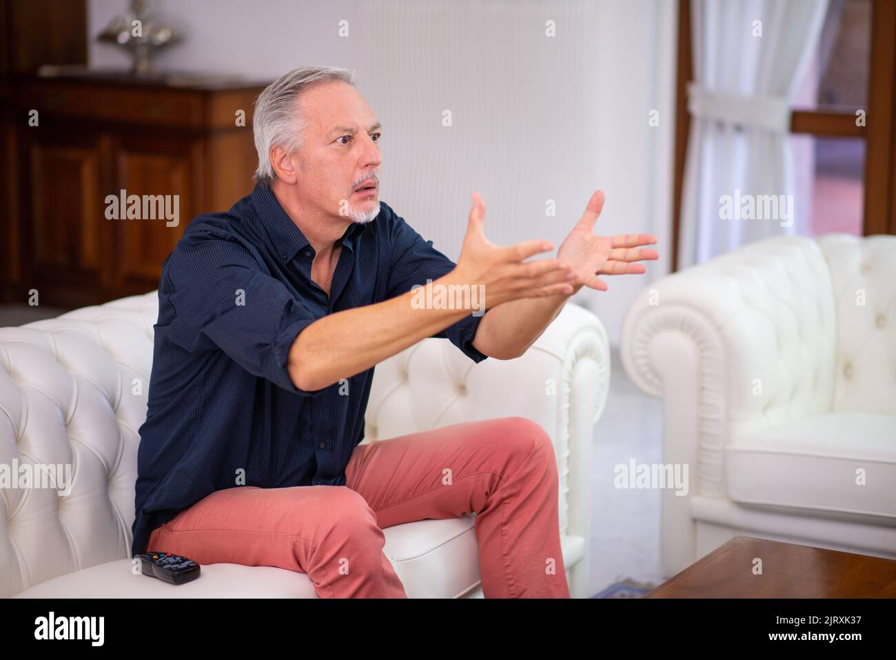 Un homme senor regarde un match de sport à la télévision et criait Banque D'Images