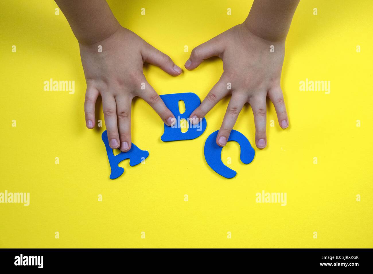 Les mains des enfants tiennent des lettres. Lettres bleues sur fond jaune Banque D'Images