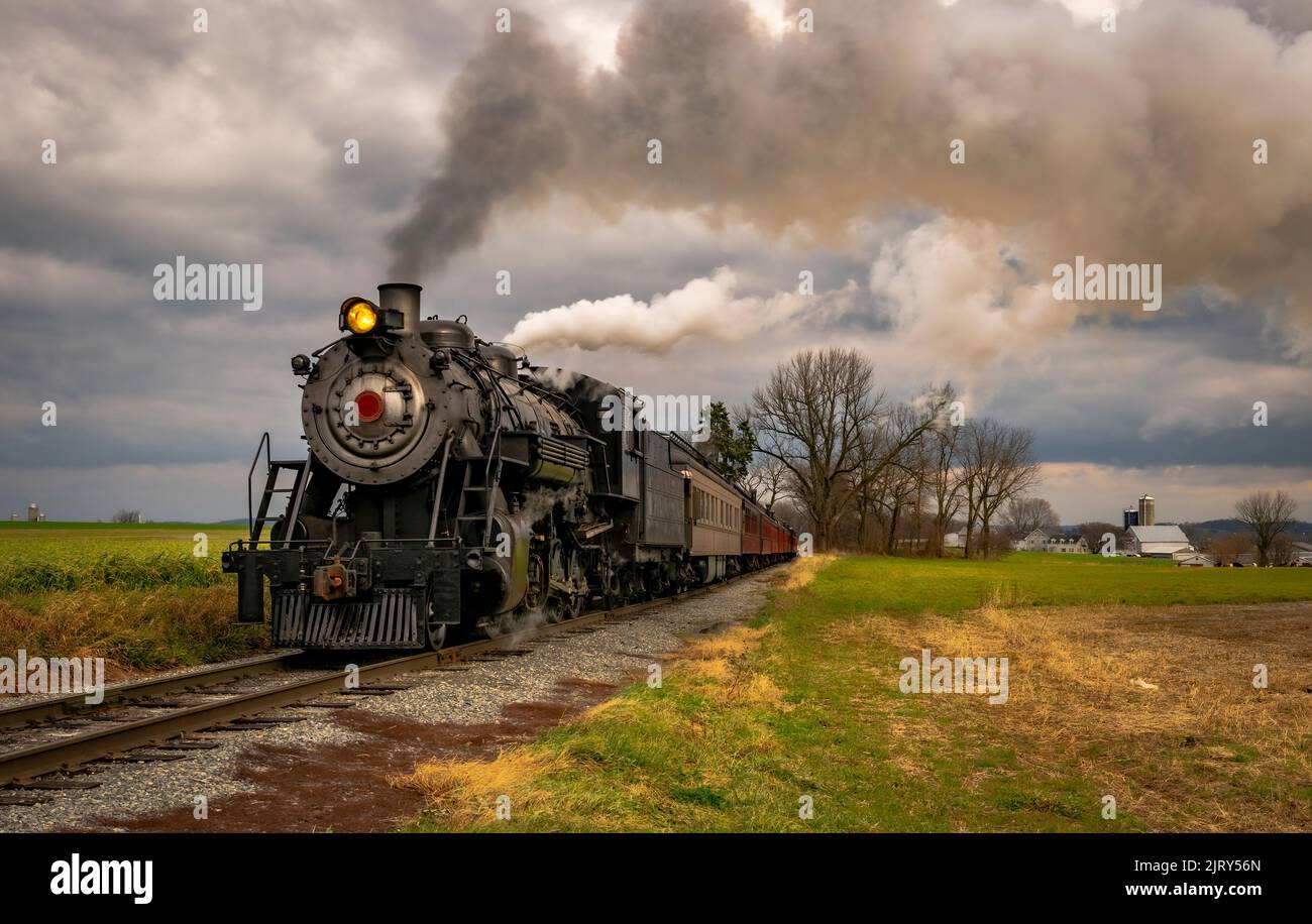 Vue rapprochée d'un train de passagers à vapeur qui s'approche à travers les terres agricoles lors d'une journée d'hiver nuageuse Banque D'Images