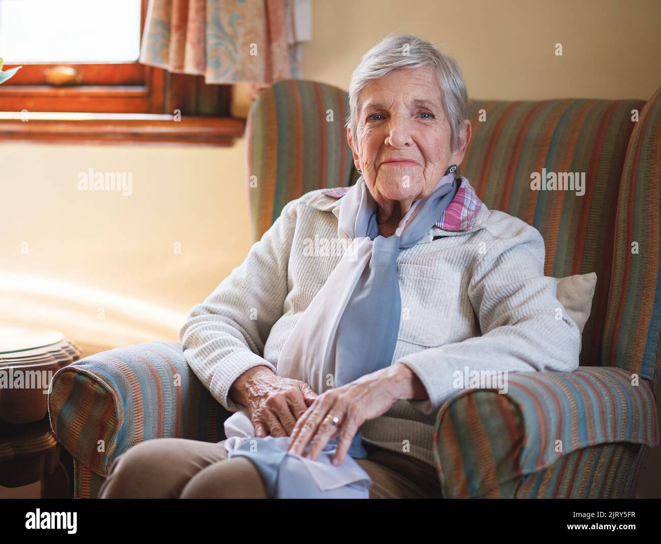 Heureuse femme âgée souriante assise sur un canapé à la maison en appréciant la retraite Banque D'Images