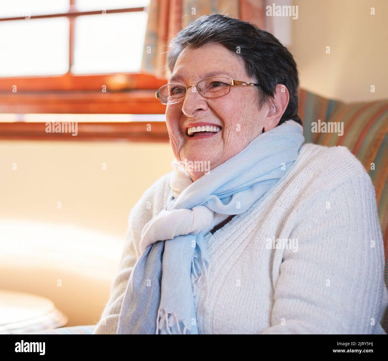 Heureuse femme âgée riant assis sur un canapé à la maison appréciant la retraite Banque D'Images