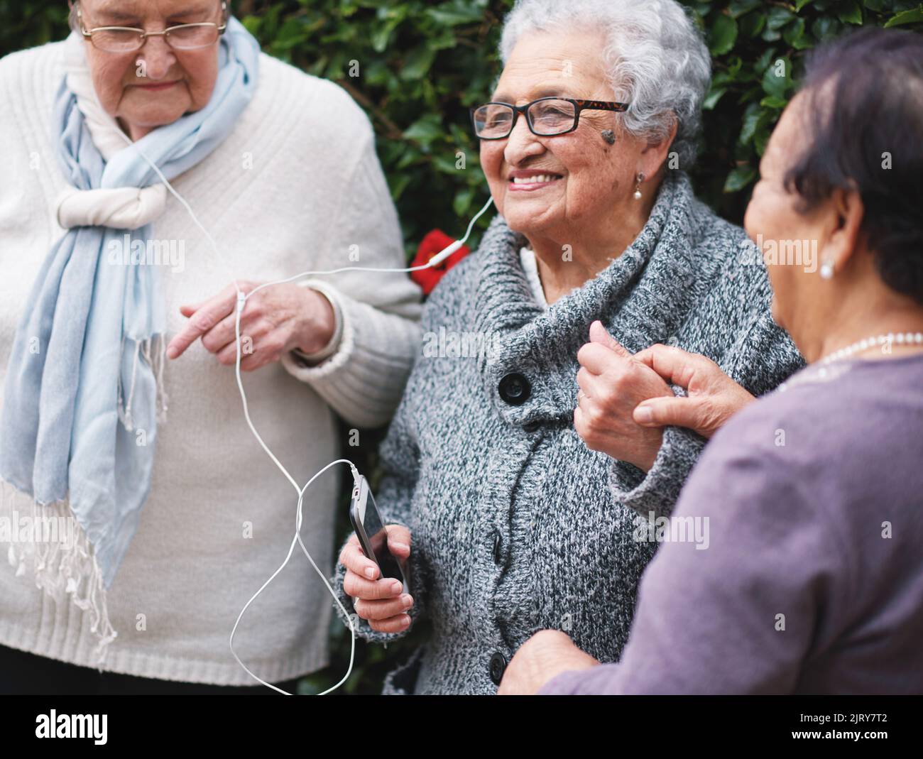Les vieilles femmes joyeuses qui écoutent de la musique sur leur smartphone portent des écouteurs souriants et s'amusent à célébrer leur retraite ensemble en plein air Banque D'Images
