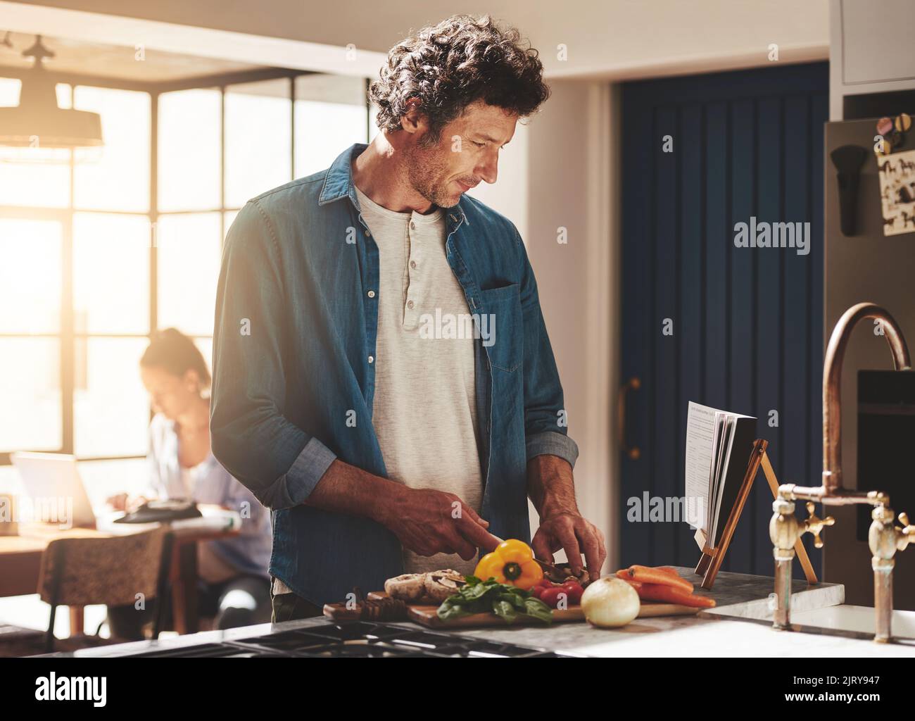 Expérimente avec une nouvelle recette. Un homme lisant une recette tout en hacher des légumes dans sa cuisine. Banque D'Images