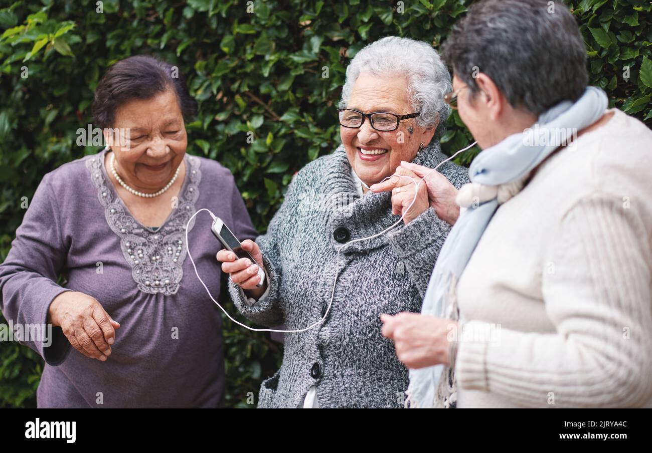 Les vieilles femmes joyeuses qui écoutent de la musique sur leur smartphone portent des écouteurs souriants et s'amusent à célébrer leur retraite ensemble en plein air Banque D'Images