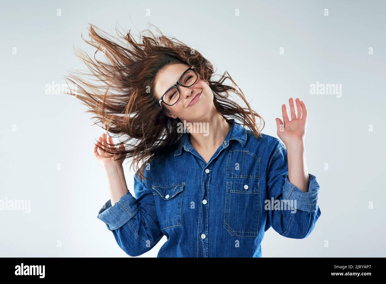 Mettez vos mains dans l'air et battez vos cheveux. Photo studio d'une jeune femme qui se retourne ses cheveux sur un fond gris. Banque D'Images