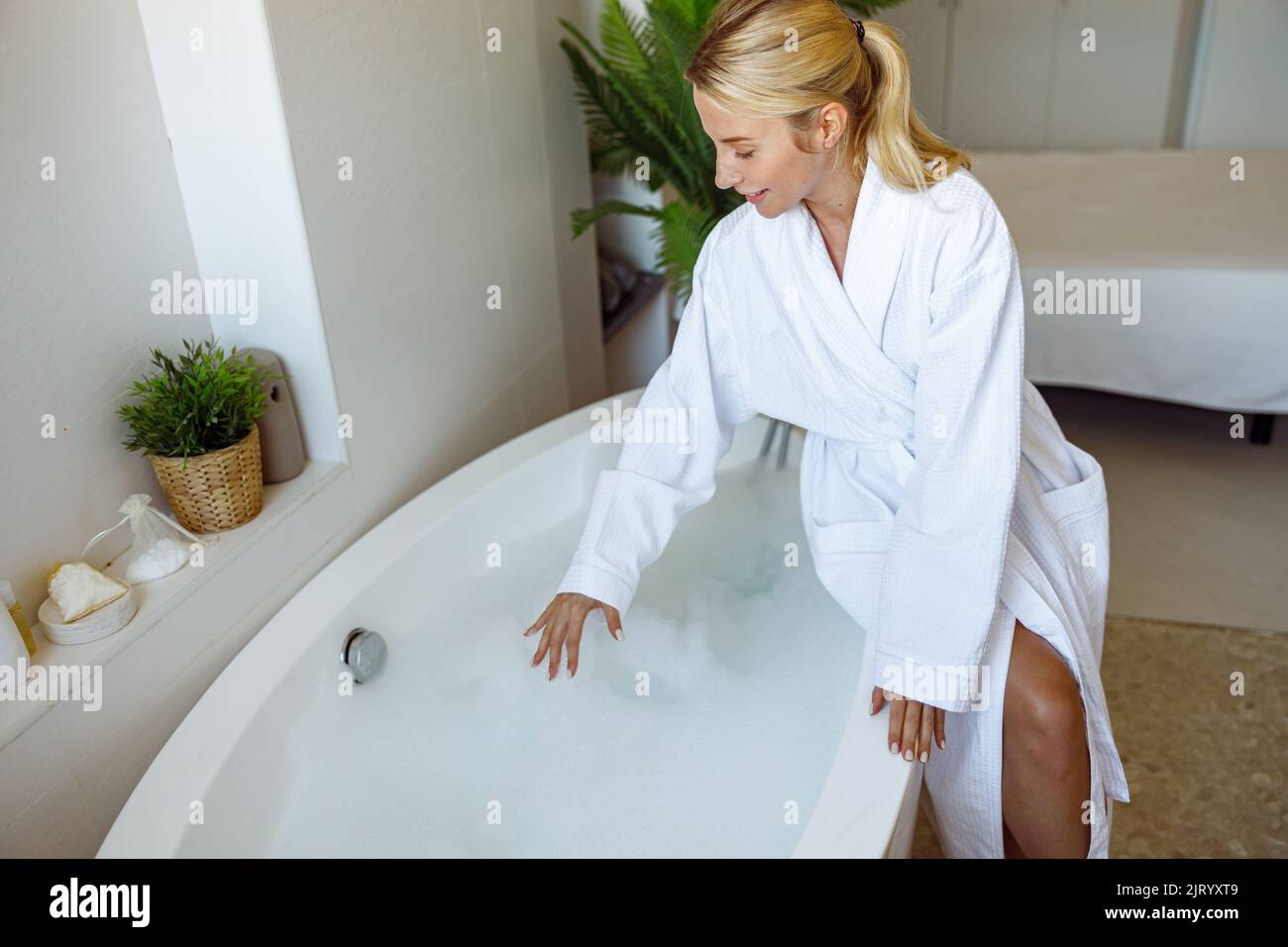 Vue d'en haut sur une jeune femme blonde assise dans la salle de bains et préparant le bain avec des bulles. Banque D'Images