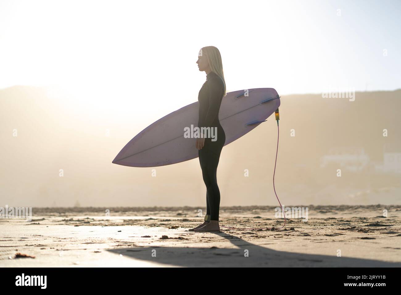 Surfeuse sur la plage debout avec sa planche de surf au coucher du soleil. Surfeuse féminine Banque D'Images