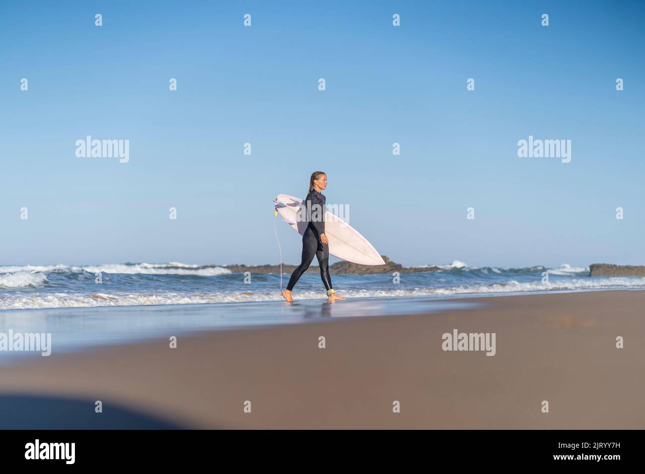 Une fille surfeuse à la plage marche avec sa planche de surf le matin. Femme surfeuse Banque D'Images