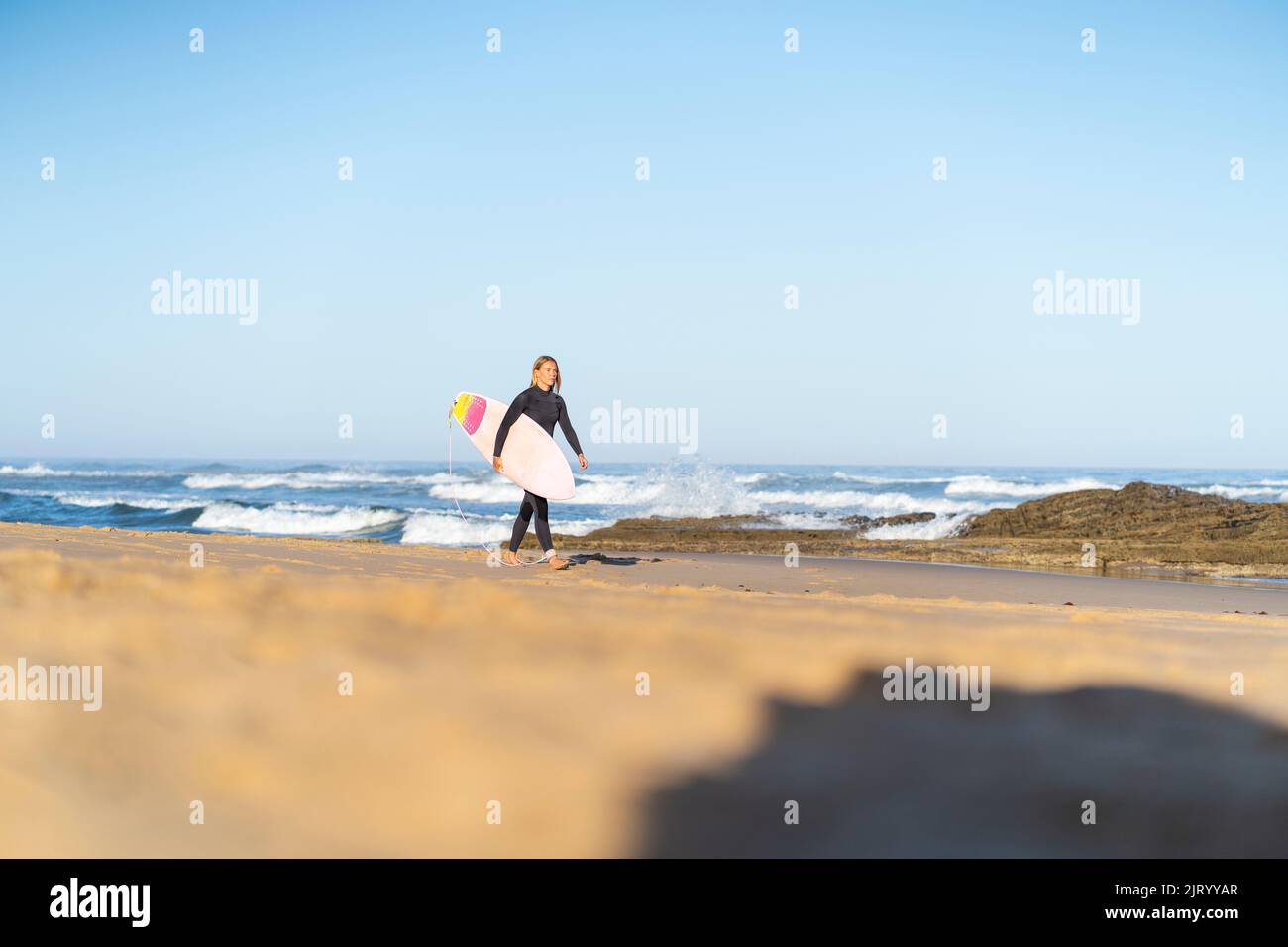 Surfeuse à la plage marchant avec sa planche de surf le matin. Femme surfeuse Banque D'Images