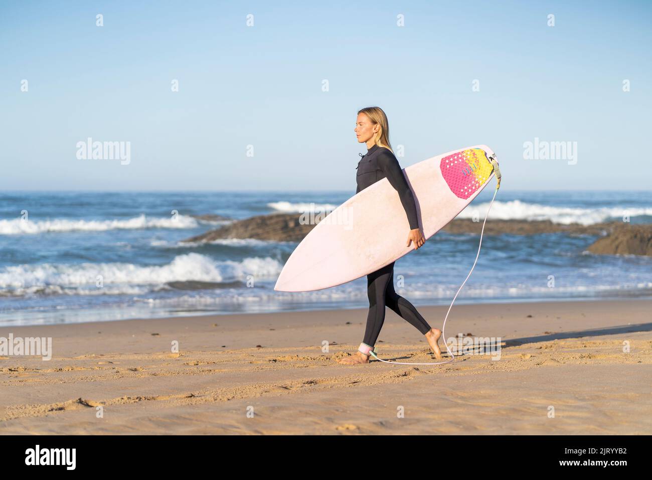 Une fille surfeuse à la plage marche avec sa planche de surf le matin. Femme surfeuse Banque D'Images