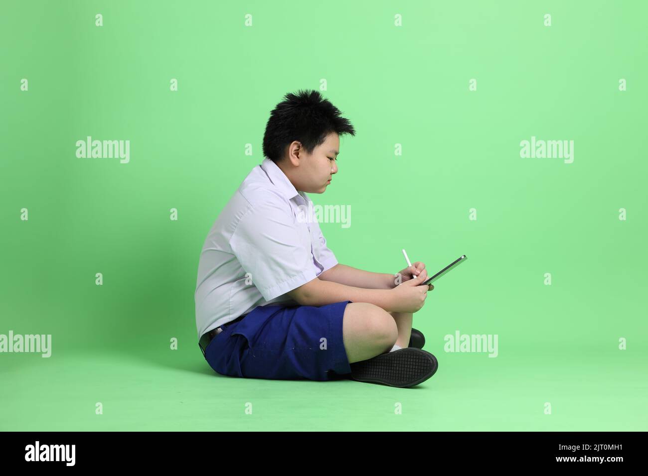 Le garçon asiatique avec l'uniforme étudiant sur fond vert. Banque D'Images