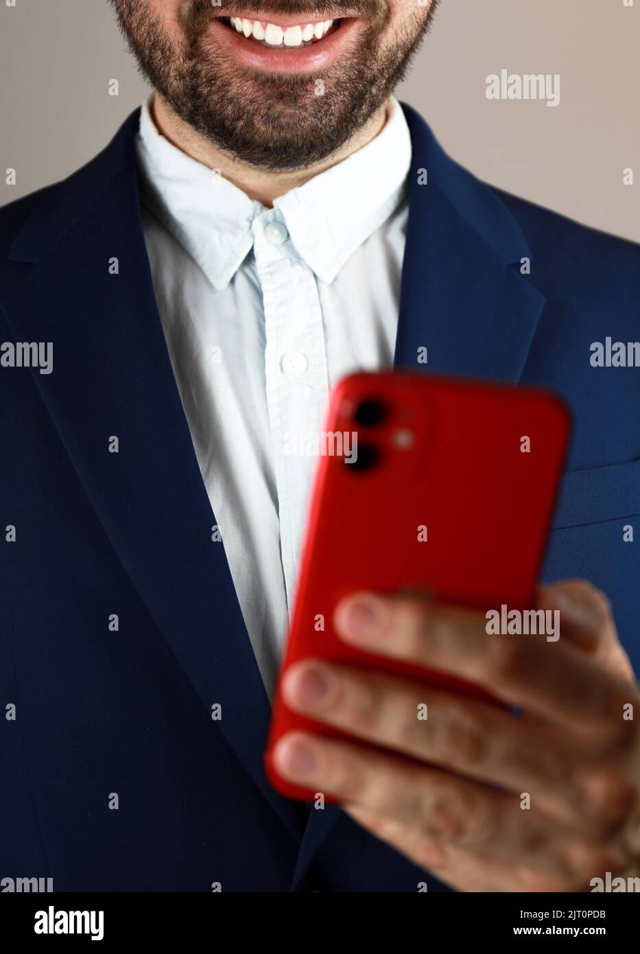 Un homme en costume tenant son téléphone rouge et souriant Banque D'Images