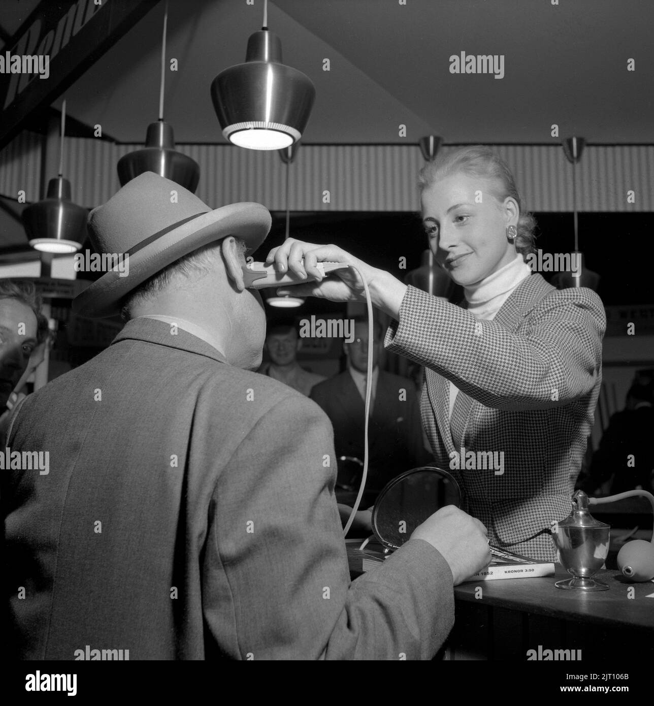 Un rasage sur le 1950s. Une jeune femme du salon St Erik à Stockholm montre le rasoir électrique à un client masculin. Suède 1952 Conard réf. 2110 Banque D'Images