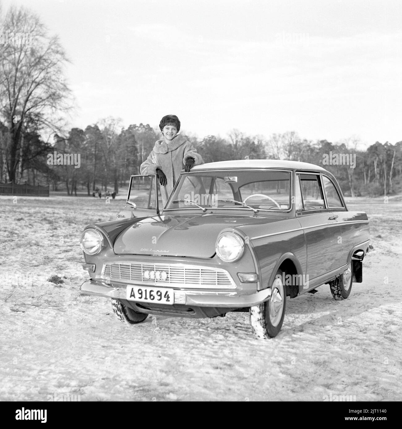 Dans le 1960s. Une jeune femme en hiver avec sa toute nouvelle voiture, une DKW Junior. Constructeur automobile allemand qui produit également des motocyclettes, faisant partie de l'Union de l'automobile. Elle a l'air heureuse et est vêtue de vêtements chauds d'hiver. Suède 1961. Banque D'Images