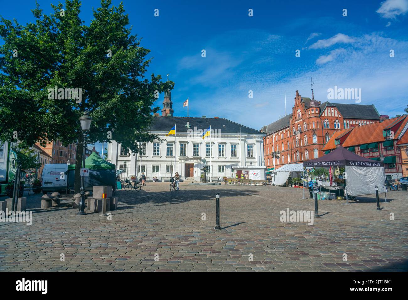 Ystad, Suède - 24, août 2022 : petite place de ville avec commerce et tentes vendant diverses choses lors d'une journée ensoleillée d'été. Gros plan avec arbres et buil Banque D'Images