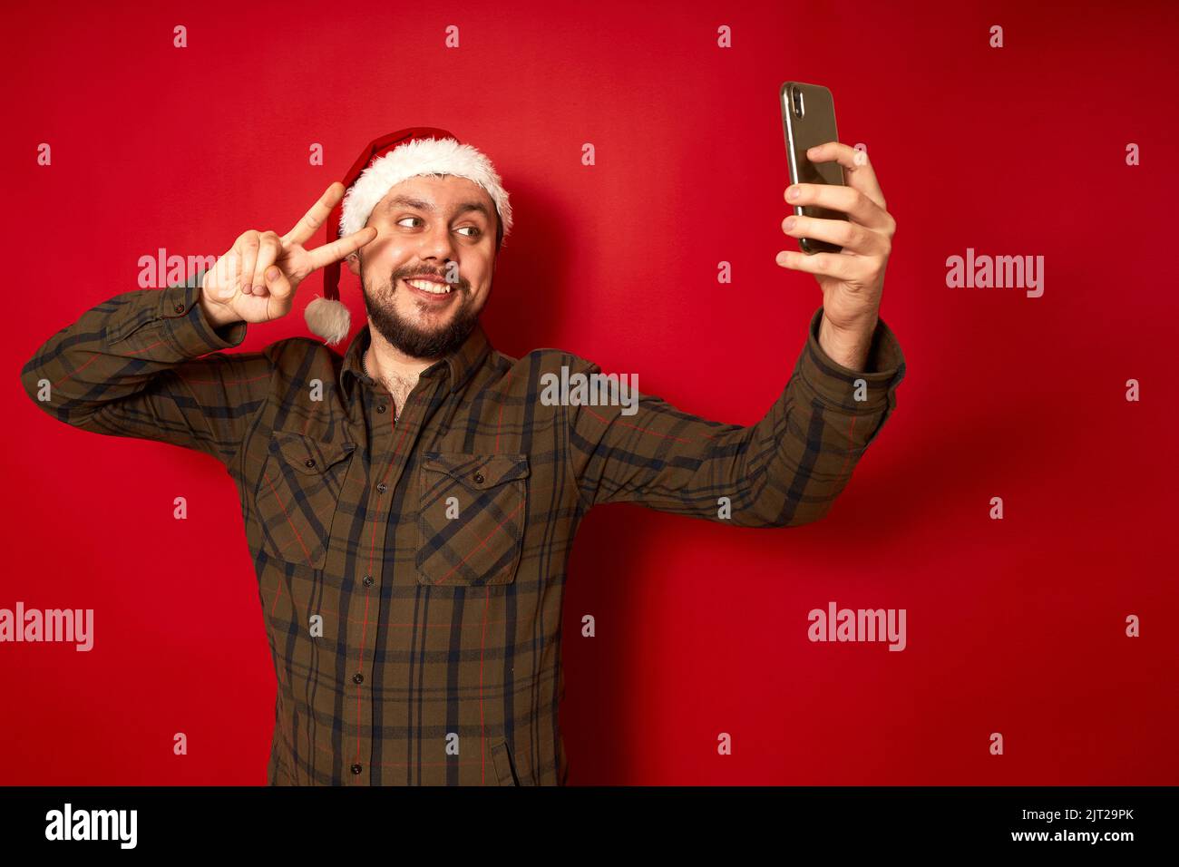 Homme souriant dans un selfie de chapeau de Noël, prend des photos de lui-même au téléphone avec la main montrant le signe de paix Banque D'Images
