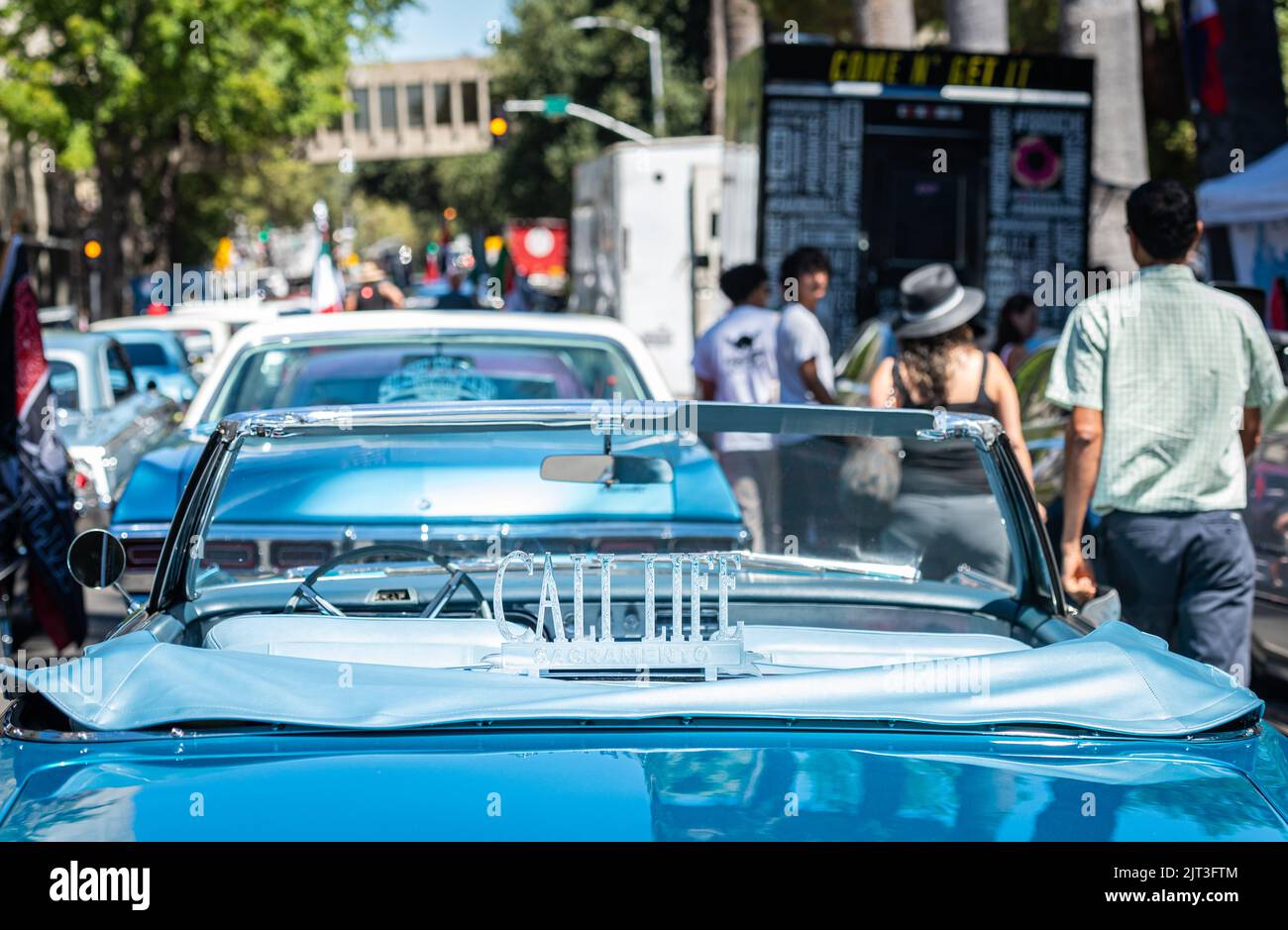 Les gens marchent devant une voiture classique bleue « lowrider » avec un panneau Cali Life au capitole de l'État dans le cadre d'une marche de l'UFW autour des droits des ouvriers agricoles. Banque D'Images