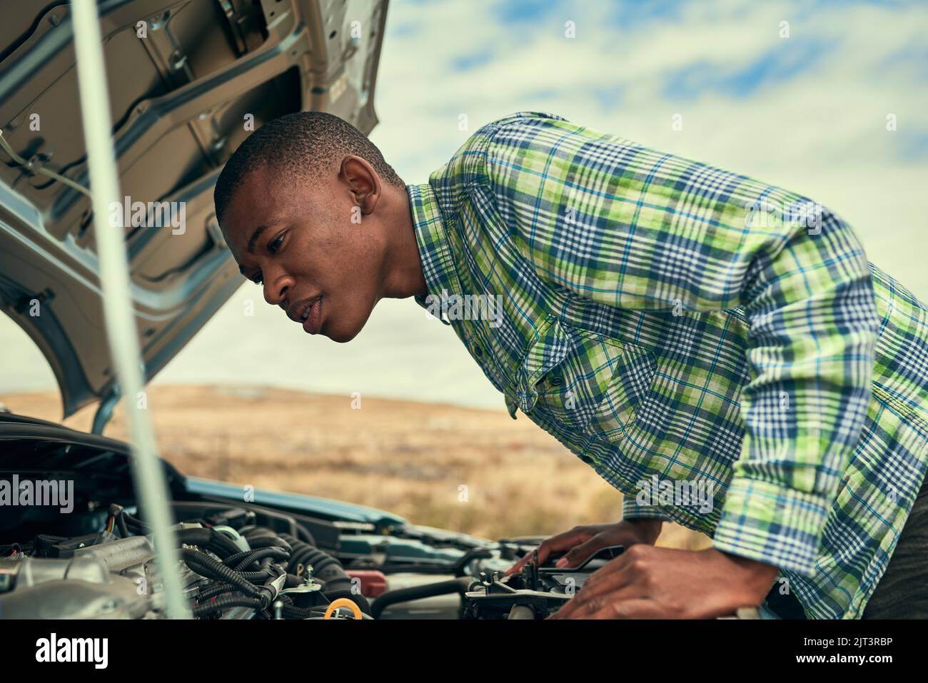 Je n'ai aucune idée de ce que je regarde... un jeune homme qui vérifie sous le capot de sa voiture après s'être défait. Banque D'Images