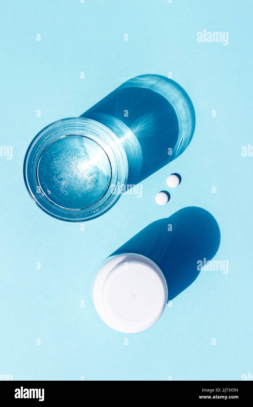 Pilules et verre d'eau sur fond bleu. Médecine, concept de soins de santé. Banque D'Images