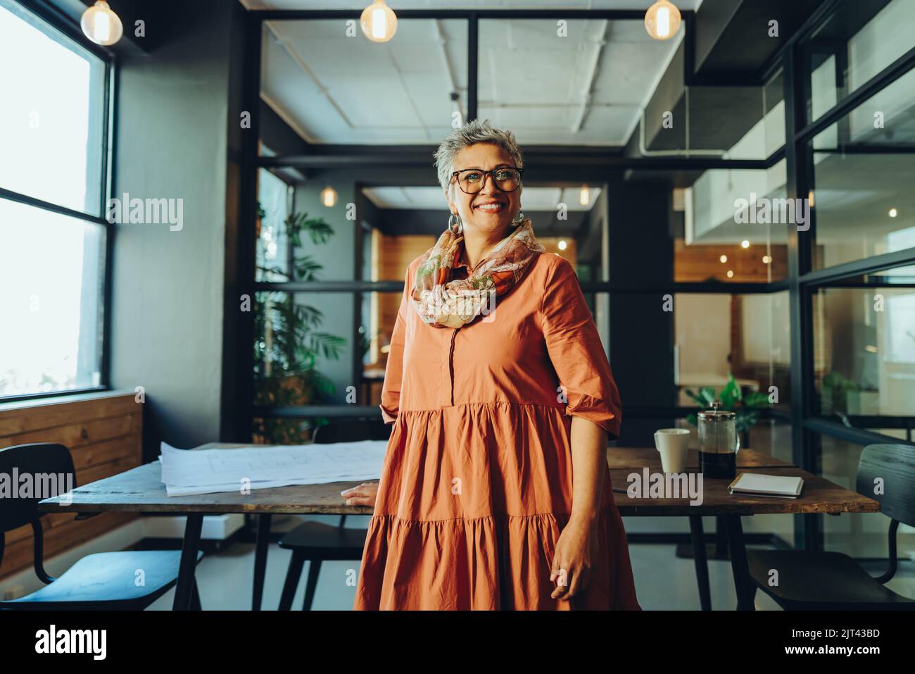 Bonne femme d'affaires mûre souriant à la caméra tout en se tenant dans un bureau. Femme d'affaires gaie et mûre debout dans la salle de réunion d'un travail moderne Banque D'Images