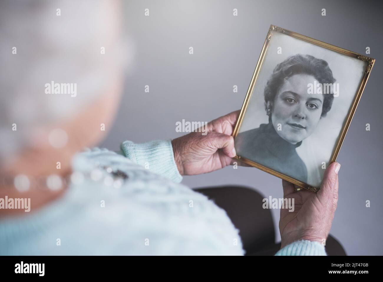 Se remémorant les années passées. Une femme âgée regardant une vieille photo noir et blanc d'une femme. Banque D'Images