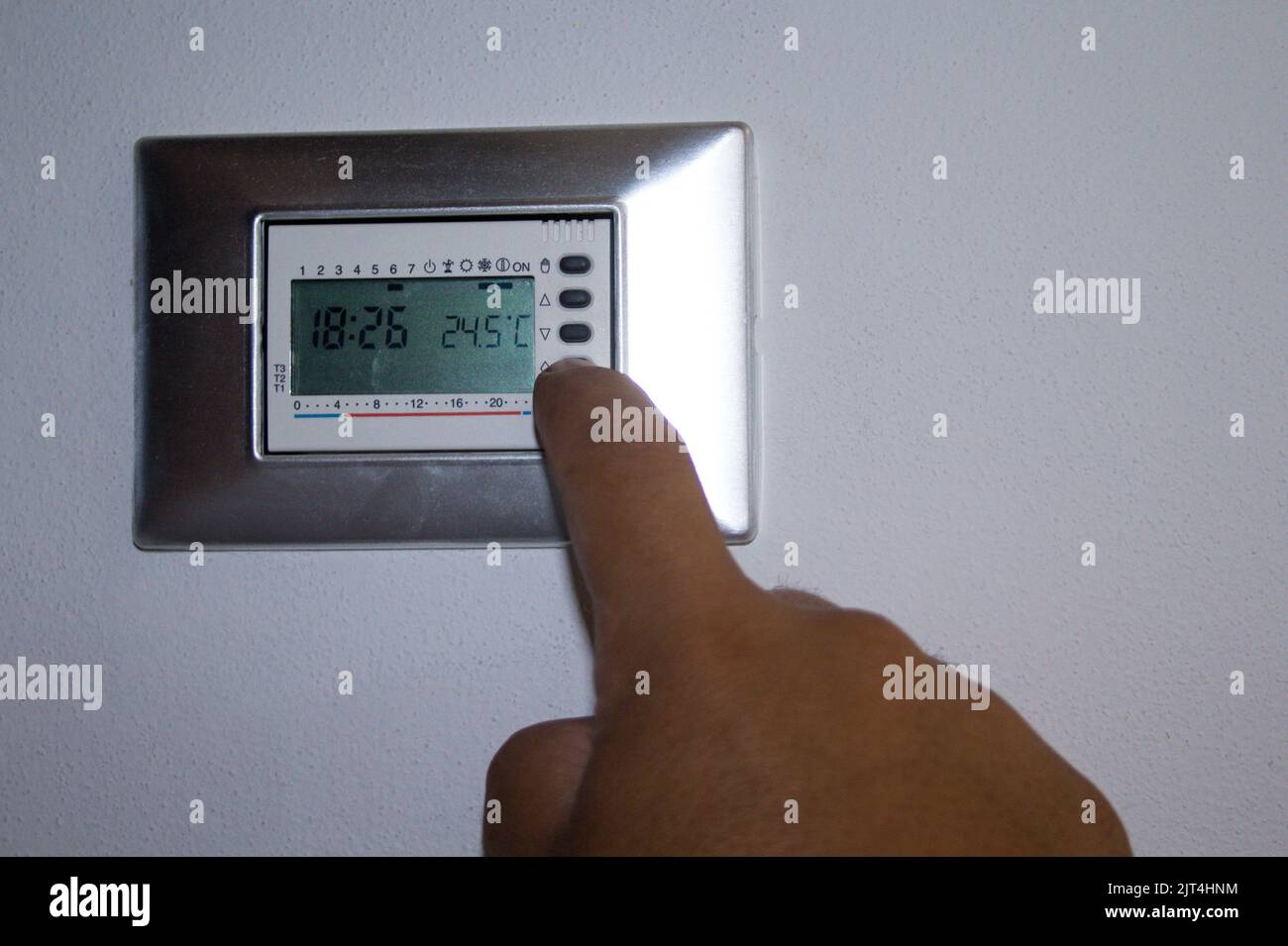 main d'un homme qui abaisse la température du thermostat de la maison avec son doigt. Référence au coût excessif, au blocage et au manque de gaz naturel Banque D'Images