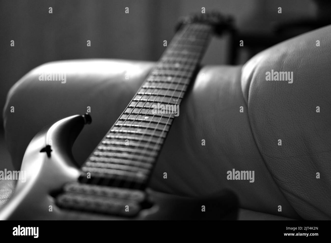 Une échelle de gris d'un cou de guitare et de fretboard sur un canapé Banque D'Images