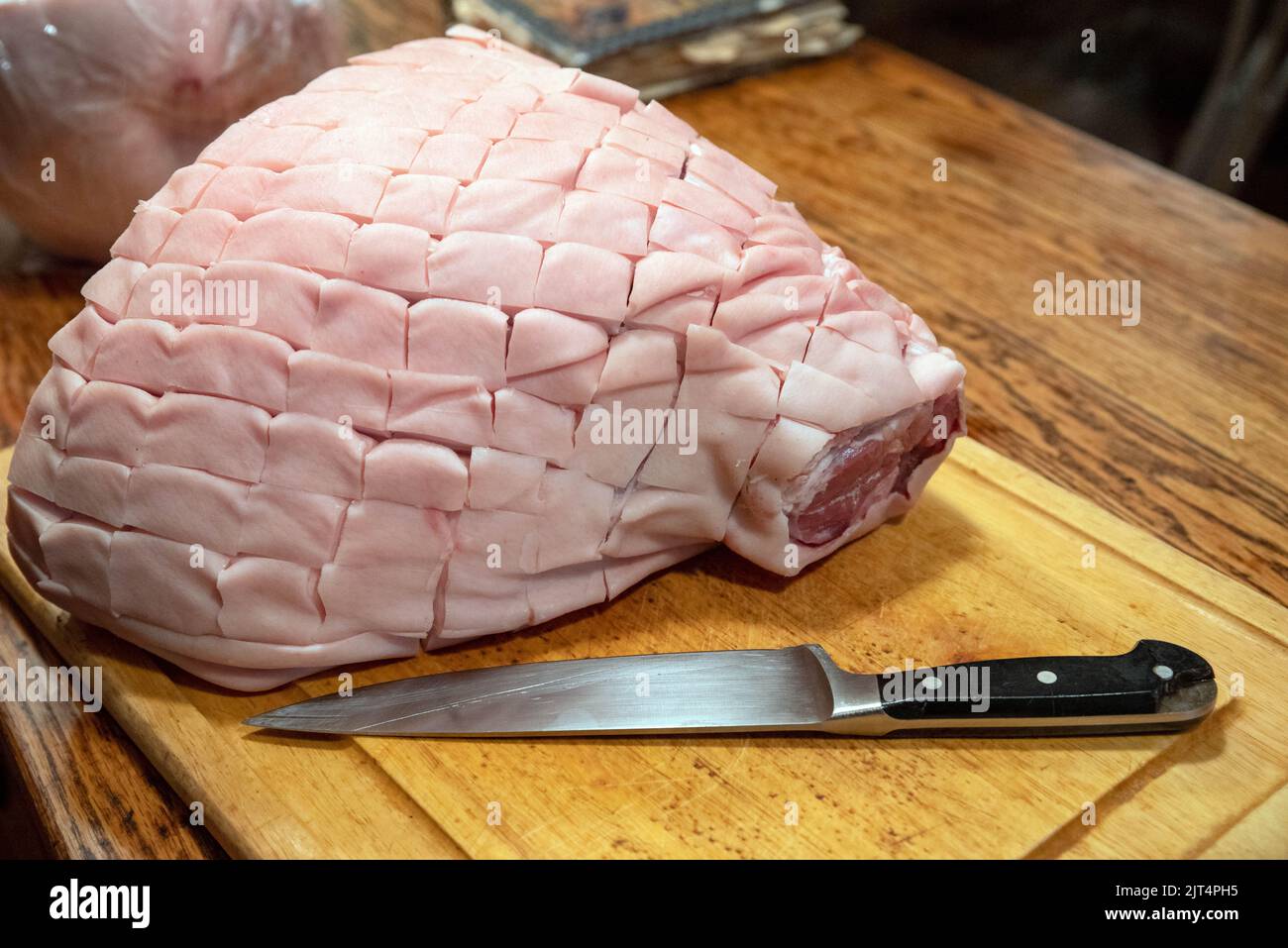 Rôti d'épaule de porc à os avec une peau hachurée sur une planche de bois avec couteau Banque D'Images