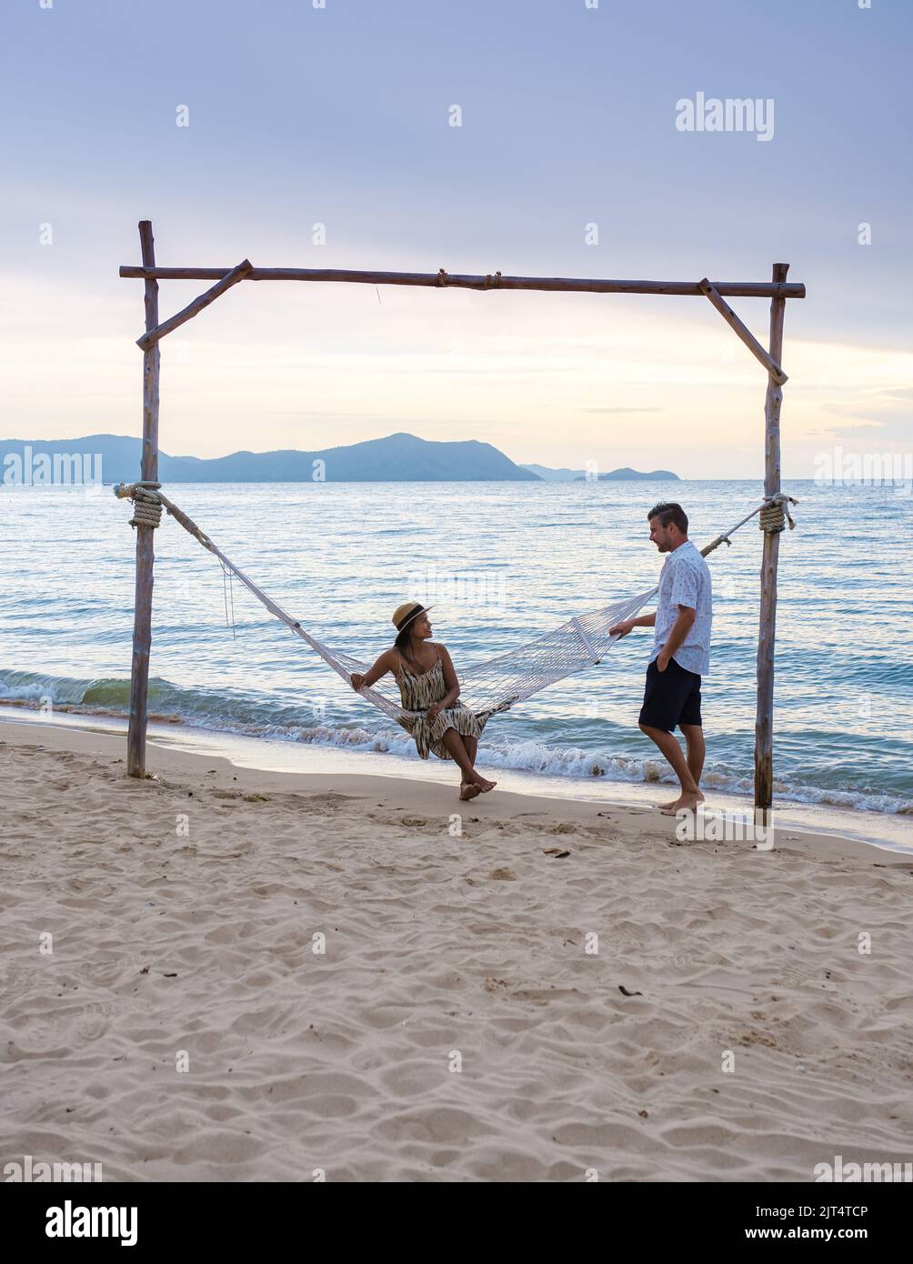 Hommes et femmes regardent le coucher du soleil depuis un hamac sur la plage de Pattaya Thaïlande Ban Amphur. Couple marchant sur une plage tropicale avec palmiers et hamac pendant le coucher du soleil Banque D'Images