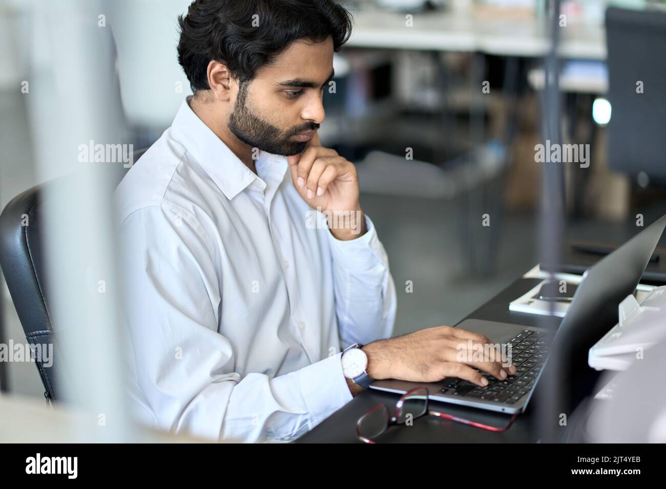Jeune employé indien occupé travaillant sur ordinateur portable, regardant l'ordinateur dans le bureau. Banque D'Images