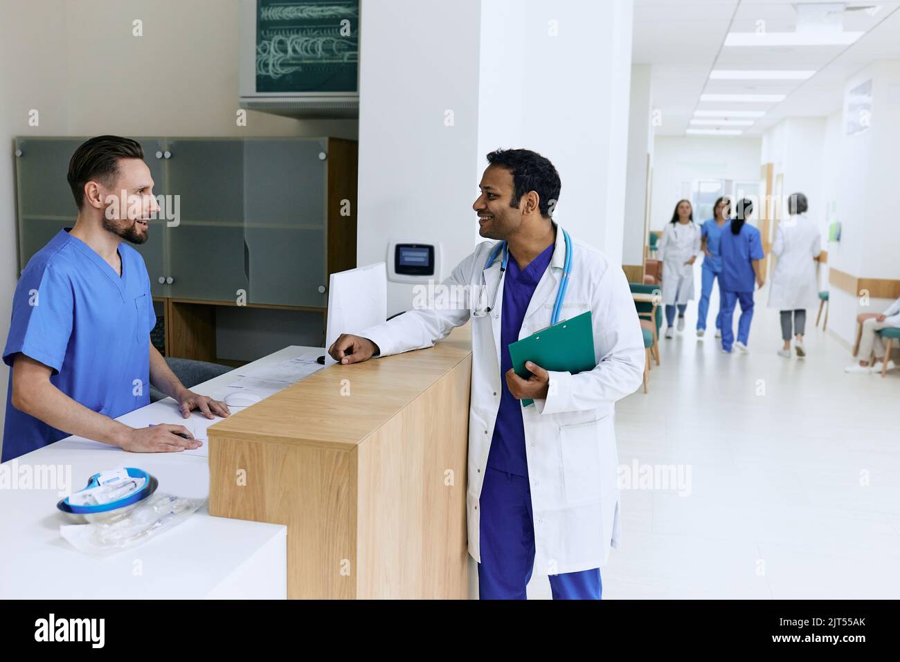 Médecin indien parlant à une infirmière masculine près du bureau de réception de l'hôpital moderne pendant la journée de travail. Vue de la clinique médicale du hall avec les patients et le p. Médical Banque D'Images