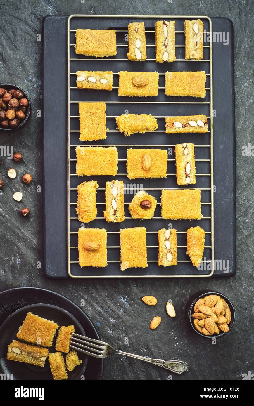 Cuisine arabe; variétés de pâtisseries du Moyen-Orient et desserts du Ramadan Kunafa placé avec des noix grillées et du miel sur fond sombre. Banque D'Images
