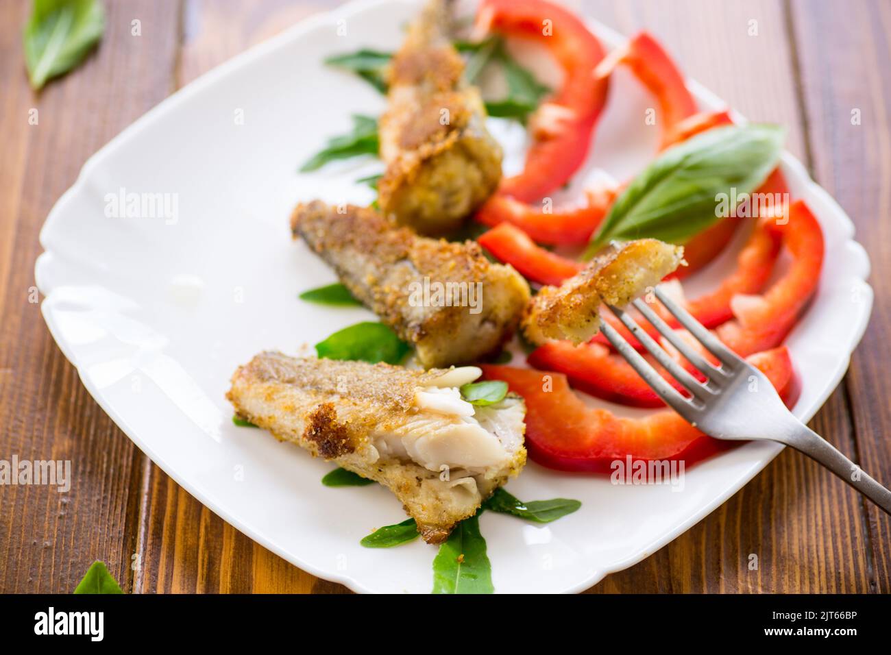 Morceaux de merlu frits dans une assiette de poivre sur une table en bois Banque D'Images