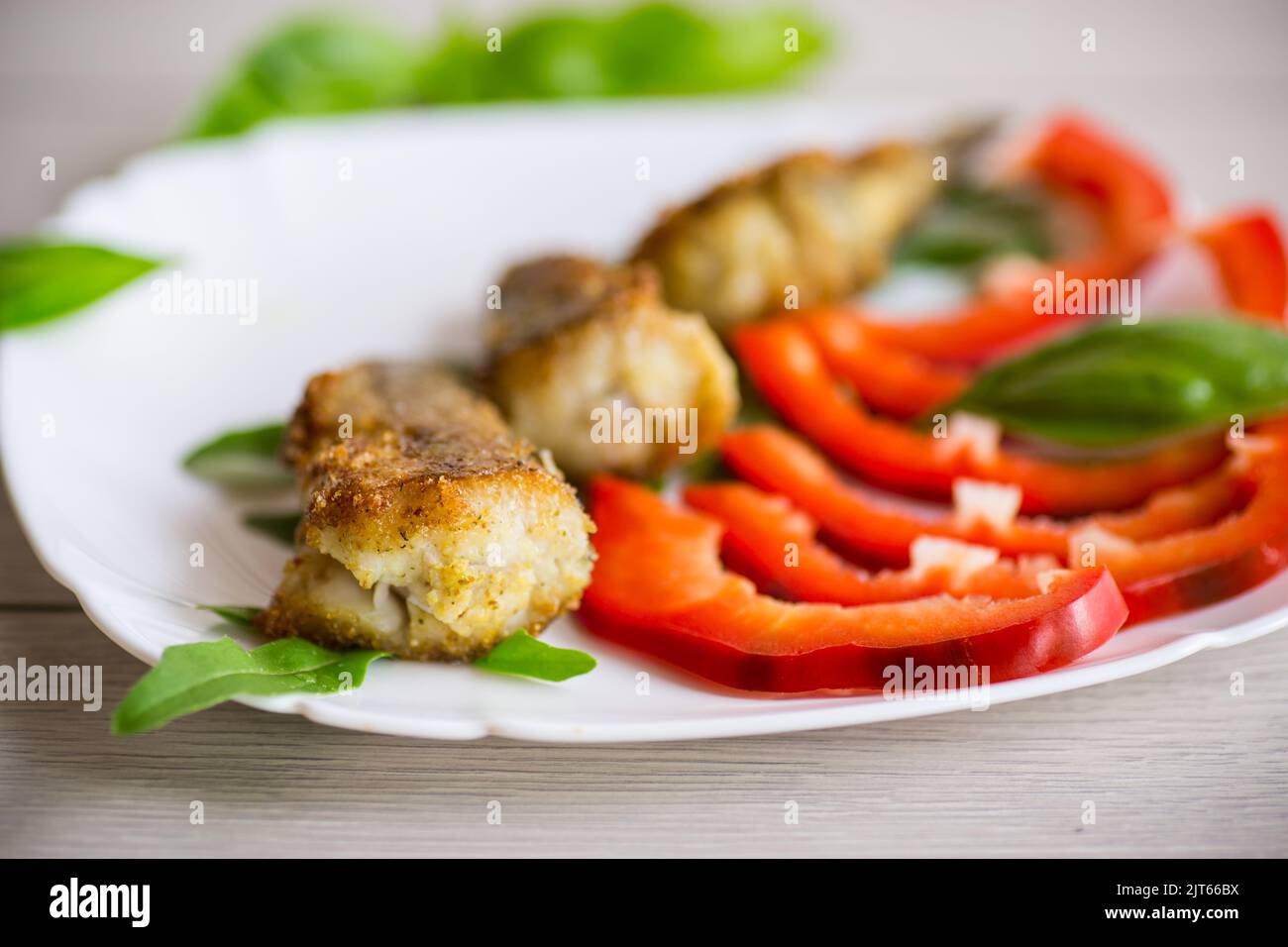 Morceaux de merlu frits dans une assiette de poivre sur une table en bois Banque D'Images