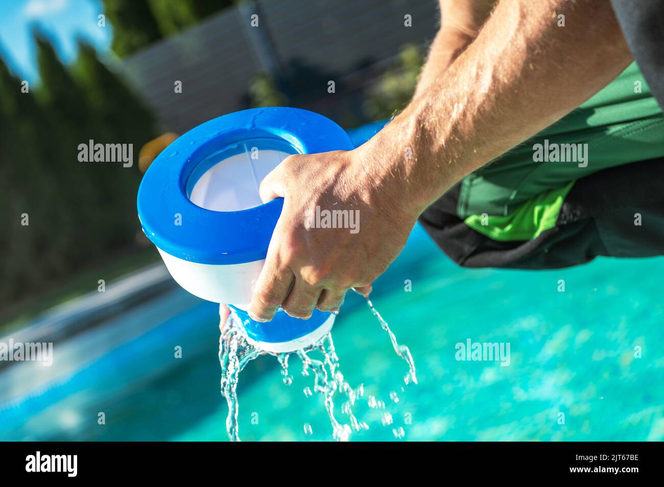 Caucasiens hommes retrait de distributeur de produits chimiques de sa piscine extérieure pour charger de nouvelles tables de chlore. Thème de traitement de l'eau. Banque D'Images