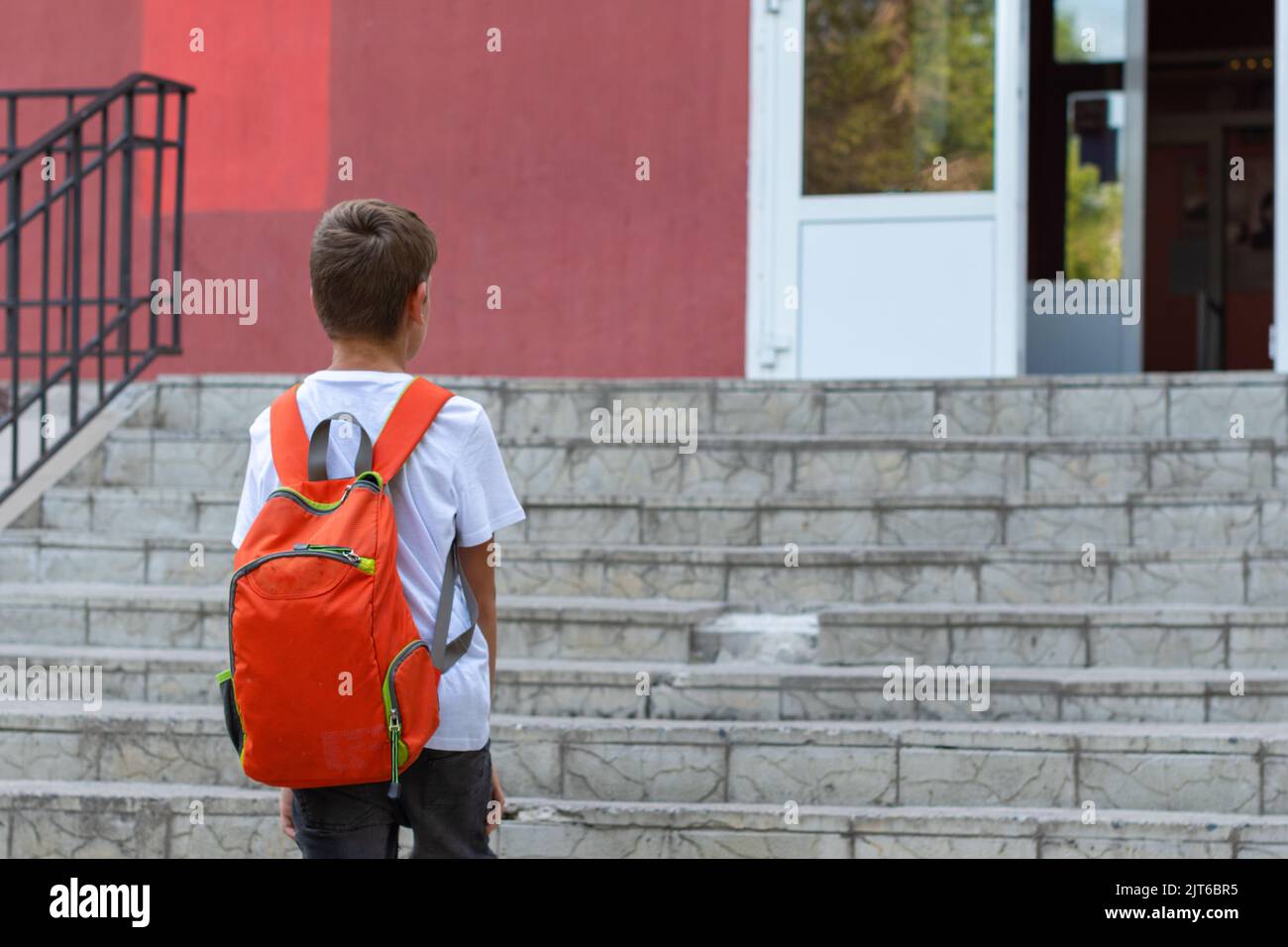 Un enfant souriant va à l'école. Vue arrière d'un garçon marchant dans les escaliers à l'extérieur de l'arrière-plan du bâtiment. Un étudiant va étudier avec un sac à dos. Arrière t Banque D'Images