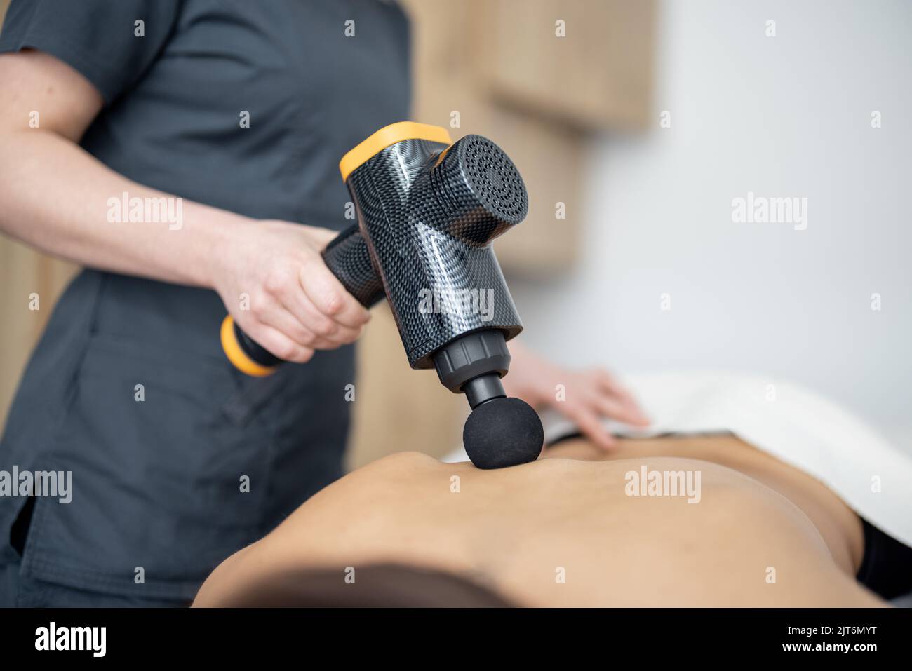 La femme fait un massage du dos du patient à l'aide d'un masseur à percussion Banque D'Images